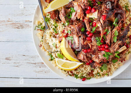 Ansicht von oben von Couscous Salat mit Petersilie langsam Braten zarte Lammkeule auseinander fallen überstieg, bestreut mit Granatapfel Samen auf einer weißen Platte mit Stockfoto