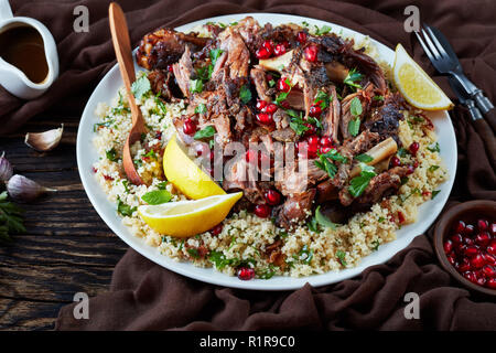 Langsam Braten fallen auseinander mit Couscous Petersilie Salat serviert, bestreut mit Granatapfel Samen, Minze auf einer weißen Platte mit Soße Blätter auf einem alten w Stockfoto