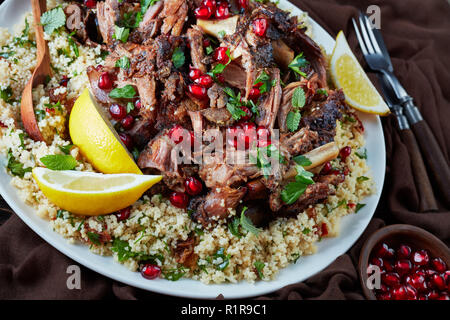 Langsam Braten fallen auseinander mit Couscous Petersilie Salat serviert, bestreut mit Granatapfel Samen, Minze auf einer weißen Platte mit Soße Blätter auf einem alten w Stockfoto