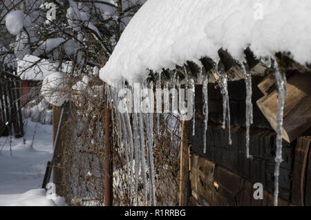 Ländliche Szene mit langer transparente Eiszapfen auf einem schneebedeckten Dach Stockfoto