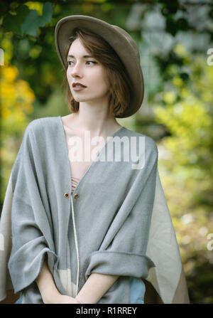 Modische junge Frau trägt in Hut und Poncho unter tropischen Pflanzen. Stockfoto