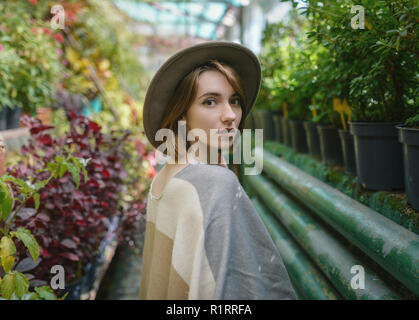 Modische junge Frau trägt in Hut und Poncho unter tropischen Pflanzen. Stockfoto