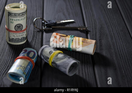 Zwei Rollen von hundert-Dollarscheine, ein 50-roll roll, ein 20-Euro roll mit Gummibänder auf einem schwarzen Holztisch vor dem Hintergrund der Tasten verknüpft Stockfoto