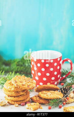 Weihnachten und Neujahr Zusammensetzung mit köstlichen peanut Cookies, Erdnüssen und Tasse Kaffee oder Tee, Niederlassungen Fichte und kiefer Kegel auf Licht Tabelle und Stockfoto