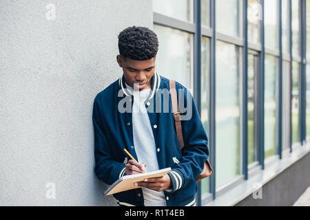 Konzentrierten jungen afrikanischen amerikanischen Studenten schreiben in Lehrbuch Stockfoto