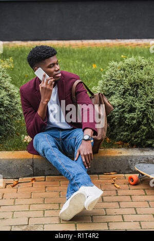 Hübscher junger Mann telefonisch beim Sitzen auf Kandare auf der Straße Stockfoto