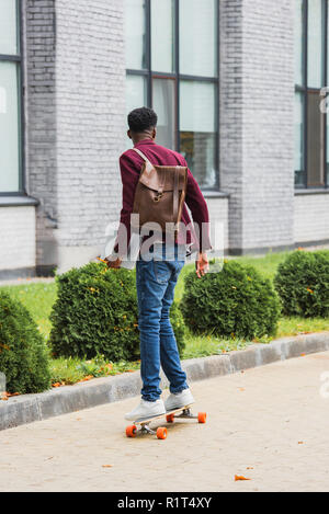 Ansicht der Rückseite des Kursteilnehmers mit Rucksack und Notebooks reiten auf Skateboard auf der Straße Stockfoto