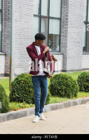 Stilvolle junger Student mit Rucksack und Notebooks stehen auf der Straße Stockfoto