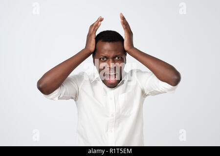 Verärgert wütend afrikanischen Mann hält die Hände vor sein Gesicht und schrie über graue Wand isoliert Stockfoto