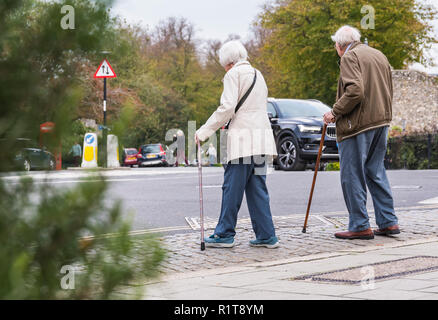 Senior paar Leute mit Stöcken Überqueren einer Straße in Großbritannien. Stockfoto