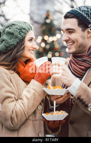 Paar mit Essen und Trinken auf Weihnachtsmarkt am jeweils anderen suchen Stockfoto