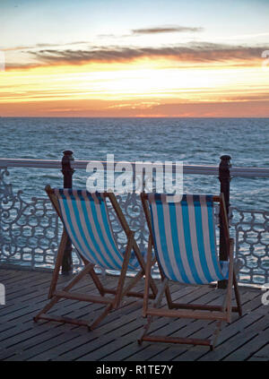 Liegestühle mit Blick auf den Sonnenuntergang am Pier in Brighton Stockfoto