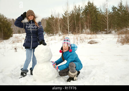 Zwei weibliche Freunde einen Schneemann bauen. lustig Mädchen auf einem Spaziergang im Winter im Freien Stockfoto