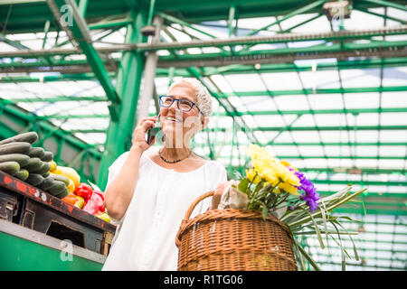 Portrait der älteren Frau kaufen Gemüse auf dem Markt und mit Handy Stockfoto