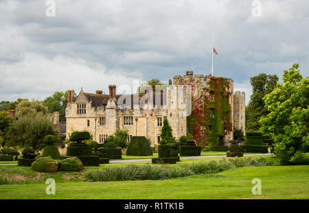 Außerdem befinden sich das Hever Castle, England, Großbritannien - 08 September 2018: Blick auf das Hever Castle und seine Formschnitt Garten an einem bewölkten Tag, mit einer Flagge bei voller Mast. Stockfoto
