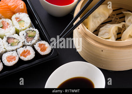 Knödel oder Gyoza in traditionellen Dampfgarer und Sushi auf schwarzem Hintergrund serviert. Nahaufnahme Stockfoto