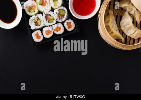 Knödel oder Gyoza in traditionellen Dampfgarer und Sushi auf schwarzem Hintergrund serviert. Ansicht von oben. Copyspace Stockfoto