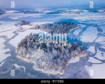 Luftaufnahme der Winter verschneite Wälder und zugefrorenen See von oben mit einer Drohne in Litauen erfasst. Stockfoto