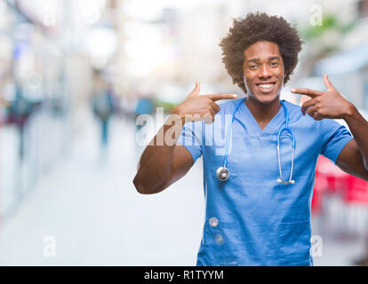 Afro-amerikanische Chirurg Arzt Mann über isolierte Hintergrund lächelt zuversichtlich zeigen und zeigen mit den Fingern Zähne und Mund. Gesundheit Konzept. Stockfoto