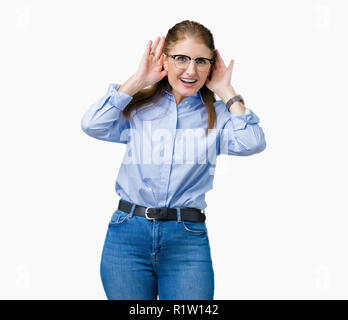 Schönen mittleren Alter reifen Business woman Brille über isolierte Hintergrund versuchen, beide Hände am Ohr Geste zu hören, neugierig, für Klatsch und Tratsch. Hören Stockfoto