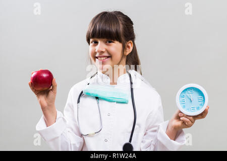 Kleine Doktor berät, ist Zeit Obst durch mit Apfel und Uhr zu essen. Stockfoto