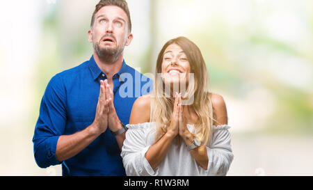 Junge Paare, die in Liebe über isolierte Hintergrund betteln und mit Händen gemeinsam beten mit der Hoffnung Ausdruck auf dem Gesicht sehr emotional und besorgt. Fragen Stockfoto