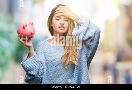 Junge hübsche blonde Frau mit Sparschwein über isolierte Hintergrund mit Hand betonte am Kopf, mit Scham und Überraschung Gesicht schockiert, wütend und f Stockfoto