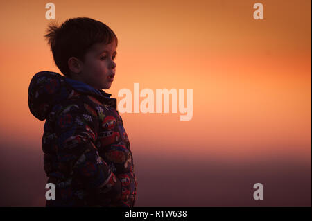 Ein vier Jahre alter Junge blickt von oben auf einem Hügel bei Sonnenuntergang von der Walliser Dorf Mossley am Mittwoch, 14. November 2018. Stockfoto