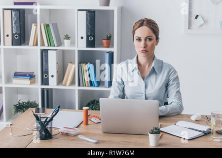 Ernst nach Geschäftsfrau mit Arzneimitteln am Arbeitsplatz bei Camera suchen Stockfoto