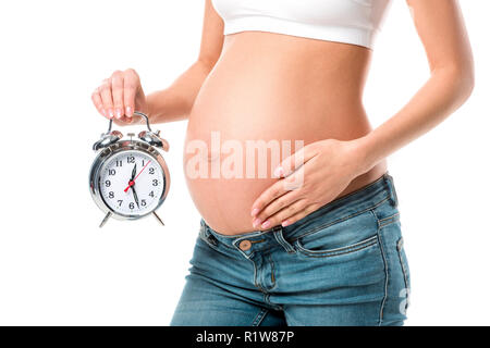 Mittelteil der schwangeren Bauch berühren und halten Wecker isoliert auf weißem Stockfoto