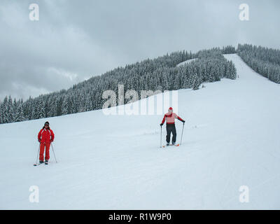 Zwei Skifahrer, ein Mann und eine Frau, in roter Kleidung auf einem Skigebiet in den Bergen Stockfoto