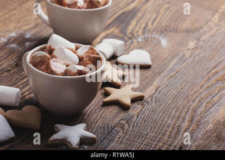 Platte von Weihnachtsplätzchen bestreut mit Puderzucker und Tassen heißer Schokolade mit Marshmallows auf hölzernen Tisch Stockfoto
