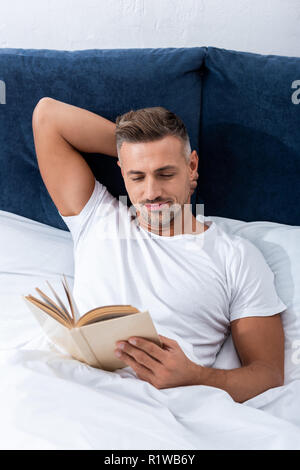 Hohe Betrachtungswinkel des Menschen lesen Buch, während im Bett während der Morgen Zeit zu Hause Stockfoto