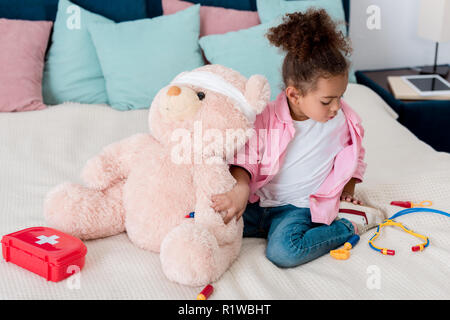 Kleine afrikanische amerikanische Kind in rosa jacke Spielen der Doktor mit Teddybär Stockfoto
