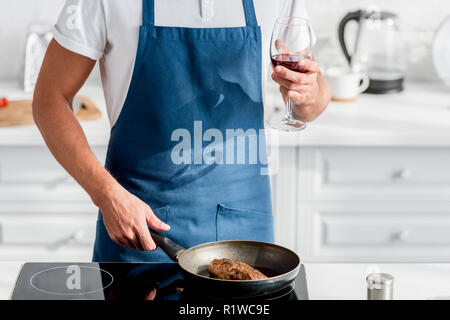 7/8-Ansicht von Mann mit Glas Wein kochen Steak auf Pan Stockfoto