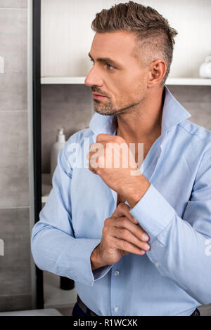 Stattliche nach Geschäftsmann, blaues Hemd zuzuknöpfen im Bad zu Hause Stockfoto