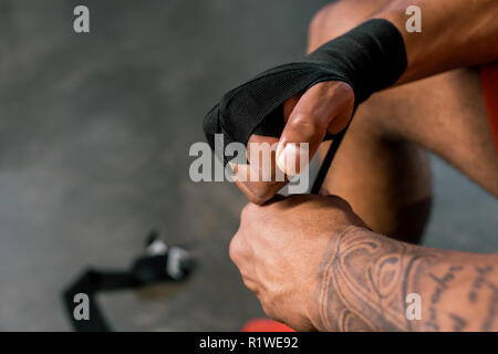 Zugeschnittenes Bild von tätowierten Sportsman Verpackung Hand in Boxing bandage im Fitnessstudio Stockfoto