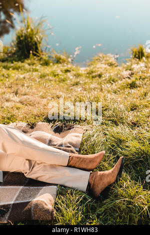 Zugeschnittenes Bild der modernen Frau in Wildleder braun Schuhe auf Gras in der Nähe von Teich im Park Stockfoto