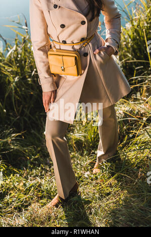 Zugeschnittenes Bild der modernen Frau in Trenchcoat mit gelber Sack im Freien posieren Stockfoto