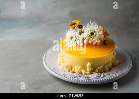 Glasierte Mango Cheesecake mit Blumen und frische Mango Stücke auf grauem Hintergrund Stockfoto