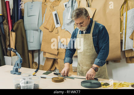 Männer mittleren Alters Handtasche Handwerker in Schürze und Brillen arbeiten mit Stoff im Studio Stockfoto