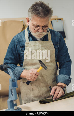 Ernste Männer mittleren Alters Handtasche Handwerker arbeiten mit Hammer im Studio Stockfoto