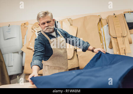 Ernste Männer mittleren Alters Handtasche Handwerker setzen Gewebe auf die Tabelle im Studio Stockfoto