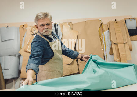 Selektiver Fokus der Männer mittleren Alters Handtasche Handwerker setzen Gewebe auf die Tabelle im Studio Stockfoto