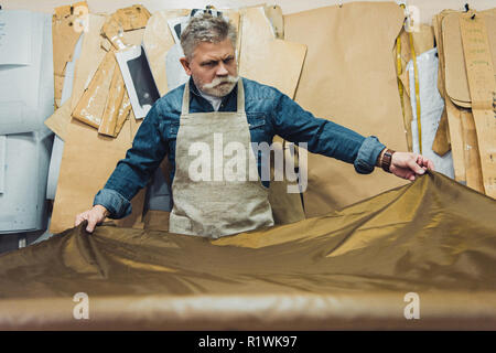 Selektiver Fokus der Männer mittleren Alters Handtasche Handwerker setzen Gewebe auf die Tabelle im Studio Stockfoto