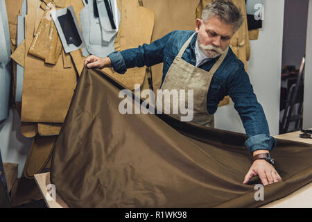 Männer mittleren Alters Handtasche Handwerker setzen Gewebe auf die Tabelle im Studio Stockfoto