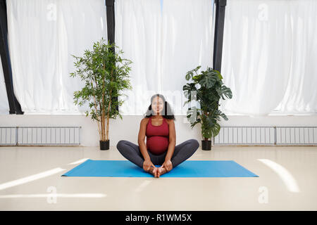 Schwangeren Yoga im Studio, sitzend auf einer Matte Stockfoto