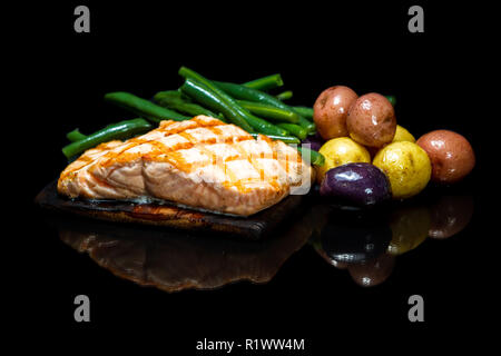 Köstliche gegrillte Lachs über eine Zeder Plank mit Baby Kartoffeln und grüne Bohnen auf einem schwarzen Hintergrund isoliert serviert. Stockfoto