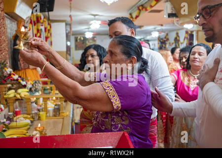 Von ihrer Familie umgeben, eine ältere Hinduistische Frau macht Angebote an die Gottheiten an einem Tempel in Ozone Park, Queens, New York. Stockfoto