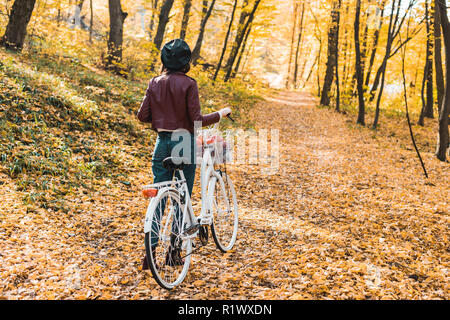 Rückansicht der Frau in stilvollem Leder Jacke und Baskenmütze mit Fahrrad im herbstlichen Wald Stockfoto